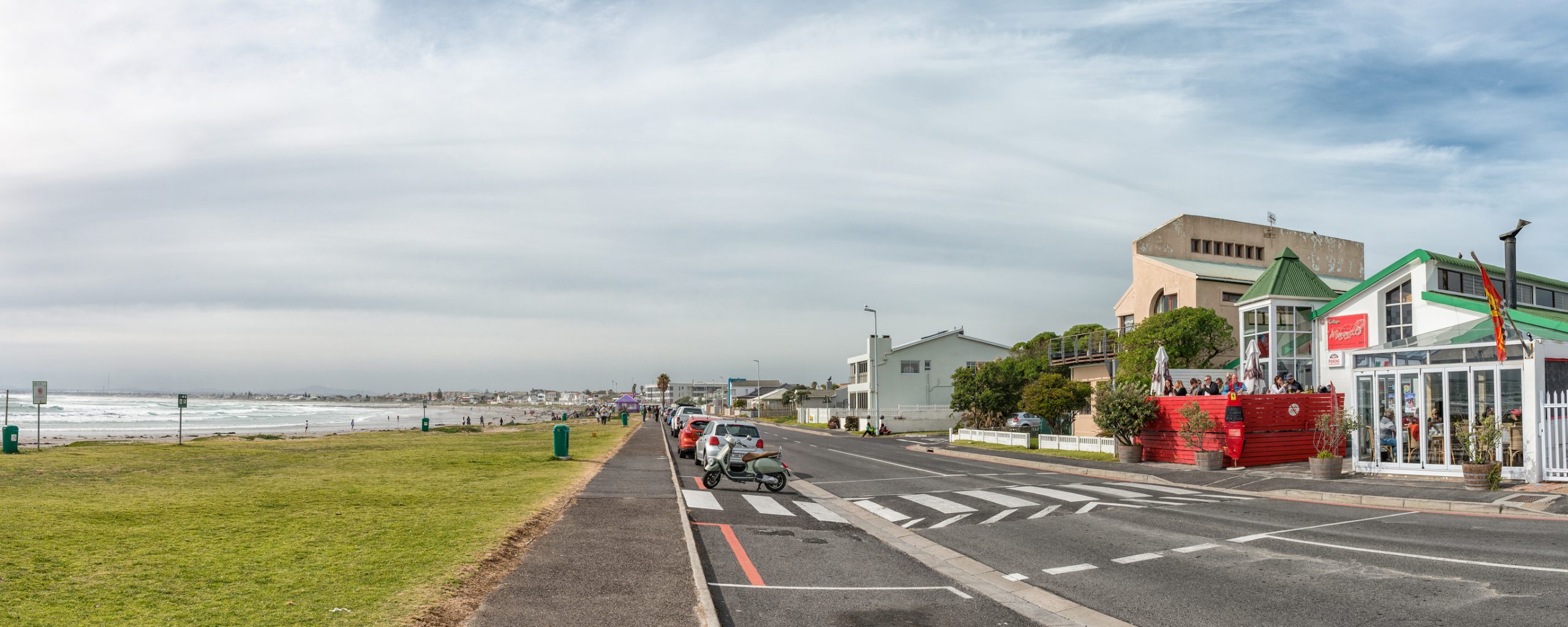 MELKBOSSTRAND, SOUTH AFRICA, AUGUST 19, 2018: A street scene, with restaurant, vehicles and people, at the beach in Melkbosstrand in the Western Cape Province
